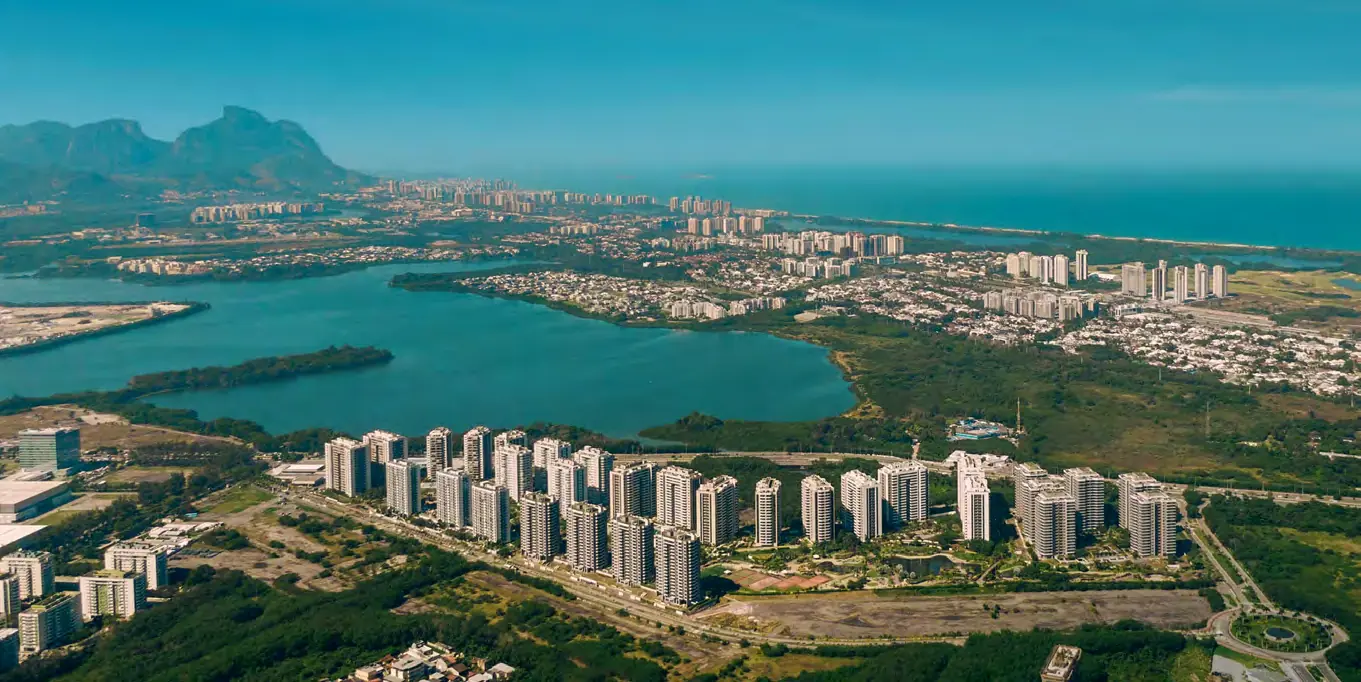 Vista aérea da região do Astra Ilha Pura, com a Lagoa de Jacarepaguá, a Barra da Tijuca, a Pedra da Gávea e o mar ao fundo